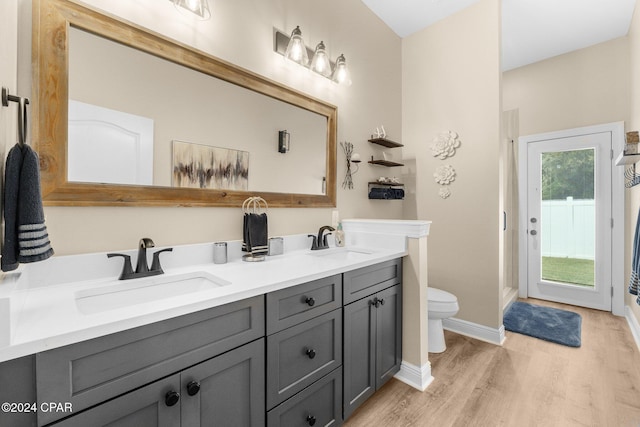 bathroom featuring double vanity, toilet, a sink, and wood finished floors