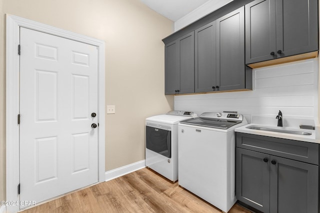 laundry room with a sink, baseboards, light wood-style floors, cabinet space, and washer and clothes dryer