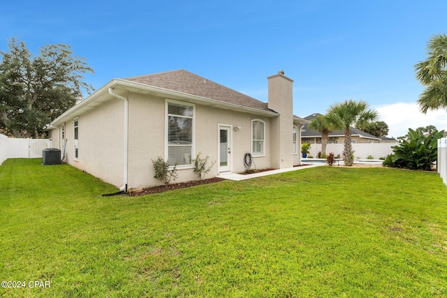 rear view of property featuring a yard, central AC unit, a fenced backyard, and stucco siding