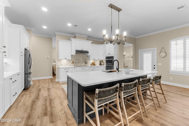 kitchen with white cabinets, appliances with stainless steel finishes, a breakfast bar, a kitchen island with sink, and pendant lighting