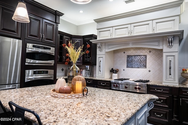 kitchen with appliances with stainless steel finishes, backsplash, light stone counters, hanging light fixtures, and crown molding