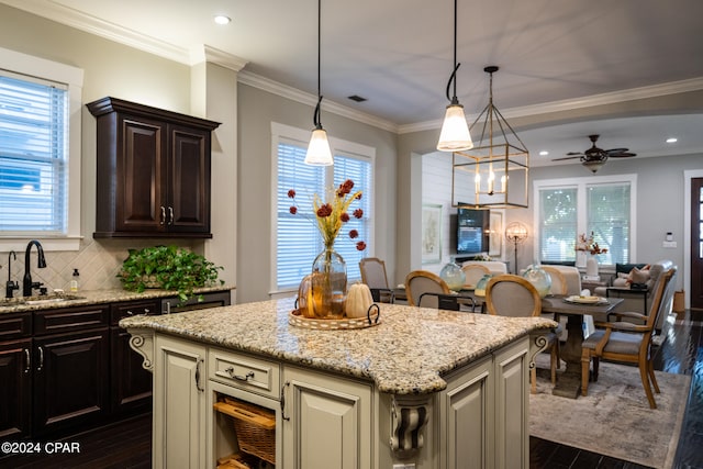 kitchen with tasteful backsplash, a kitchen island, decorative light fixtures, dark wood-type flooring, and crown molding