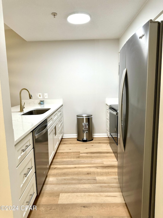 kitchen with white cabinetry, light wood-type flooring, stainless steel appliances, sink, and light stone counters