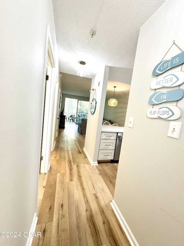 corridor with a textured ceiling and light wood-type flooring