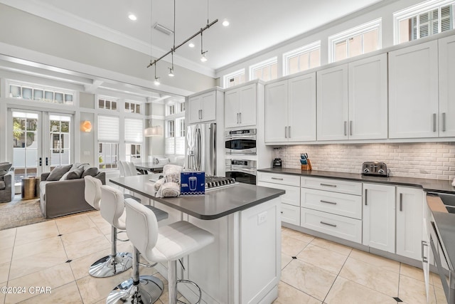 kitchen featuring a kitchen bar, stainless steel refrigerator with ice dispenser, french doors, light tile patterned floors, and white cabinetry