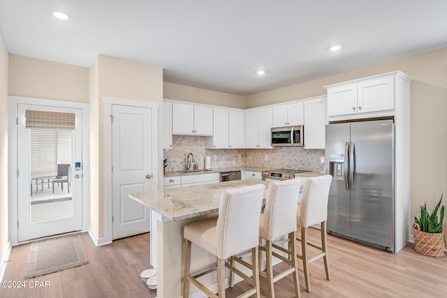 kitchen featuring sink, white cabinetry, stainless steel appliances, a center island, and light stone countertops