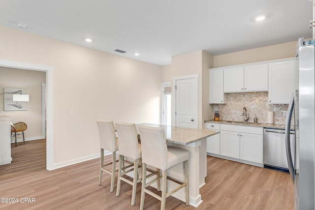 kitchen featuring dishwasher, sink, white cabinets, a center island, and light stone counters