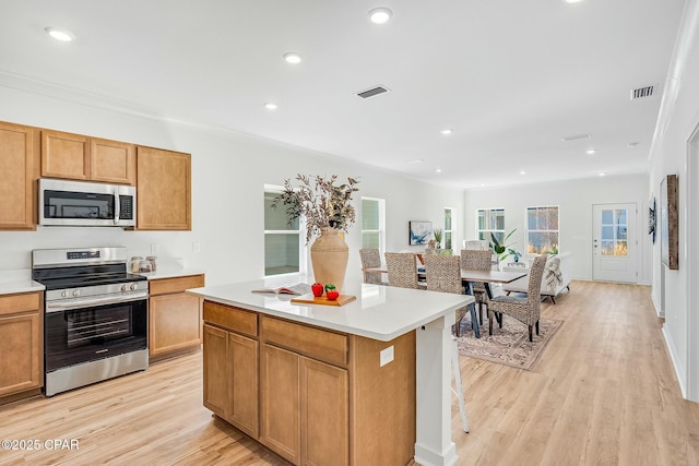 kitchen featuring appliances with stainless steel finishes, a kitchen bar, a center island, and light hardwood / wood-style floors