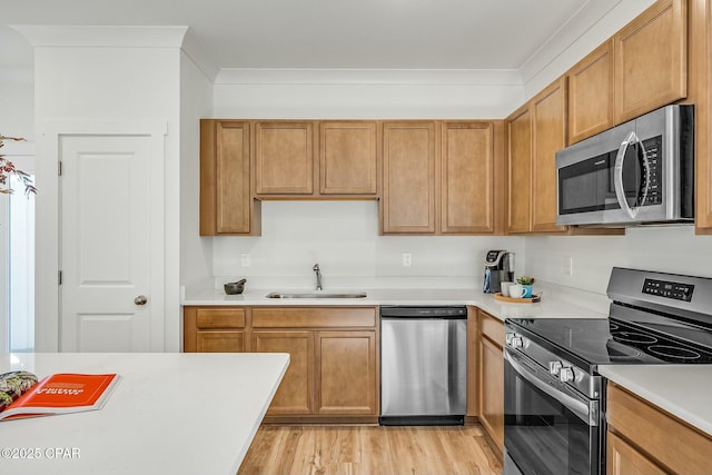 kitchen featuring ornamental molding, appliances with stainless steel finishes, sink, and light hardwood / wood-style flooring