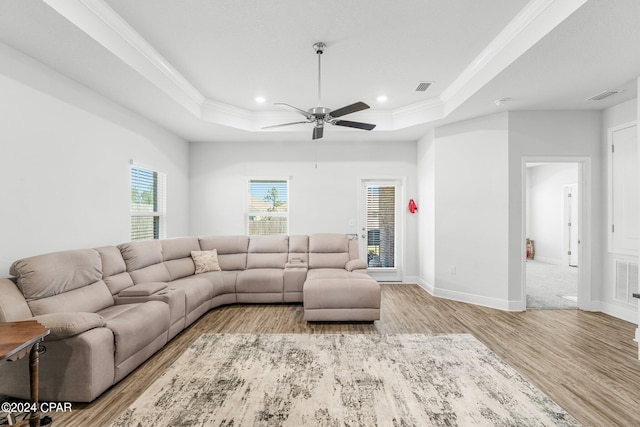 living room with crown molding, a tray ceiling, light hardwood / wood-style floors, and ceiling fan