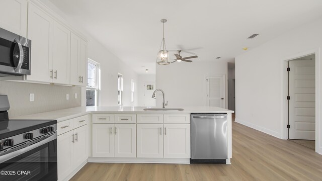 kitchen with light wood finished floors, appliances with stainless steel finishes, a peninsula, white cabinets, and a sink