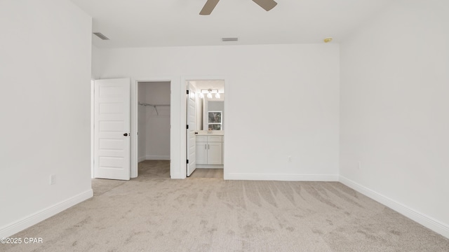 unfurnished bedroom featuring a walk in closet, light colored carpet, visible vents, and baseboards
