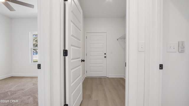 corridor with light colored carpet, light wood-type flooring, and baseboards