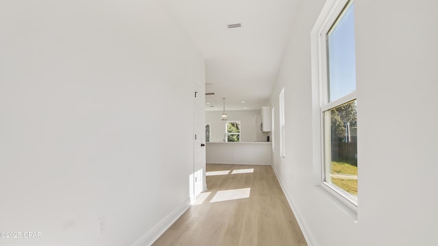 hall with visible vents, baseboards, and light wood-type flooring