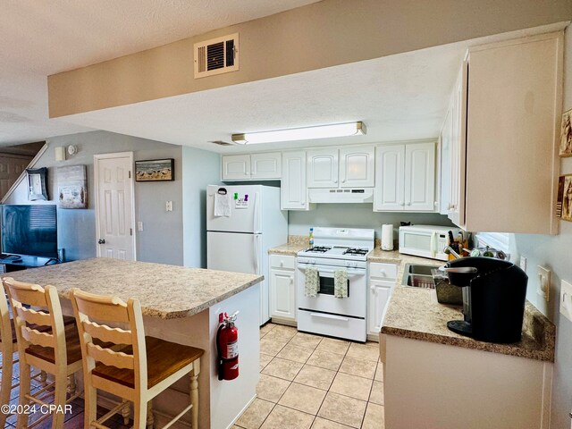 kitchen featuring a breakfast bar area, light tile patterned floors, white cabinetry, a textured ceiling, and white appliances