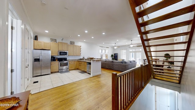 kitchen with stainless steel appliances, kitchen peninsula, light brown cabinetry, ceiling fan, and light wood-type flooring