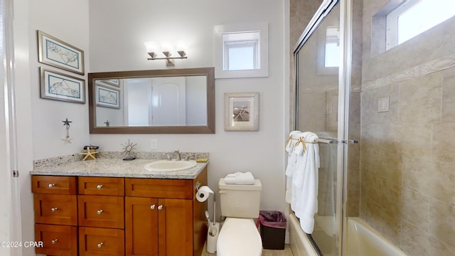 full bathroom with plenty of natural light, vanity, combined bath / shower with glass door, and toilet