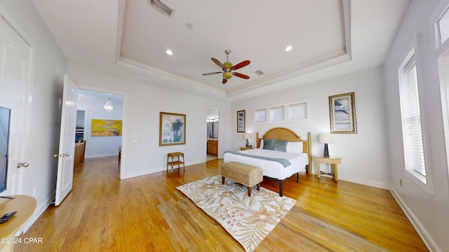 bedroom featuring light wood-type flooring, a tray ceiling, and ceiling fan