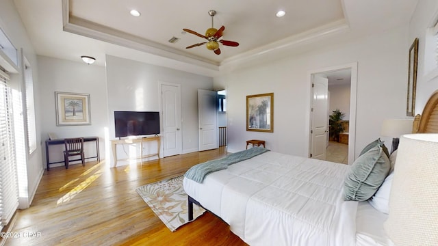 bedroom with ceiling fan, connected bathroom, light hardwood / wood-style flooring, and a tray ceiling