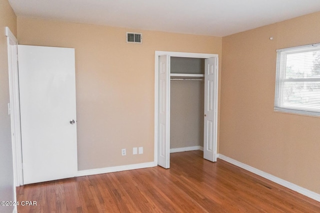 unfurnished bedroom with a closet, visible vents, baseboards, and wood finished floors