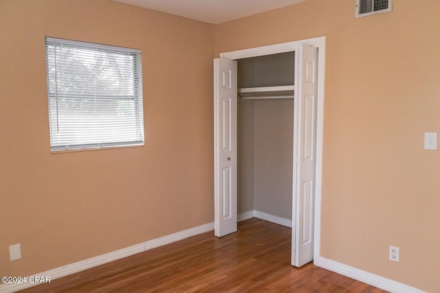 unfurnished bedroom featuring wood finished floors, visible vents, a closet, and baseboards