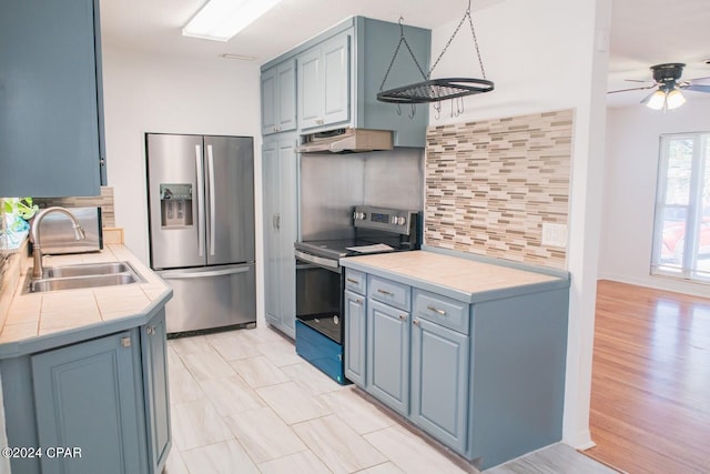 kitchen featuring sink, tile countertops, backsplash, blue cabinets, and stainless steel appliances