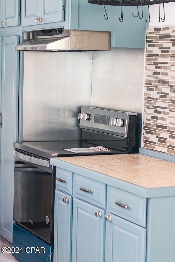 kitchen with range hood, blue cabinetry, decorative backsplash, light countertops, and electric stove