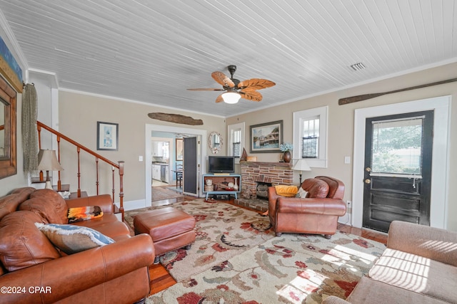 living room with ceiling fan, a stone fireplace, crown molding, and light hardwood / wood-style flooring