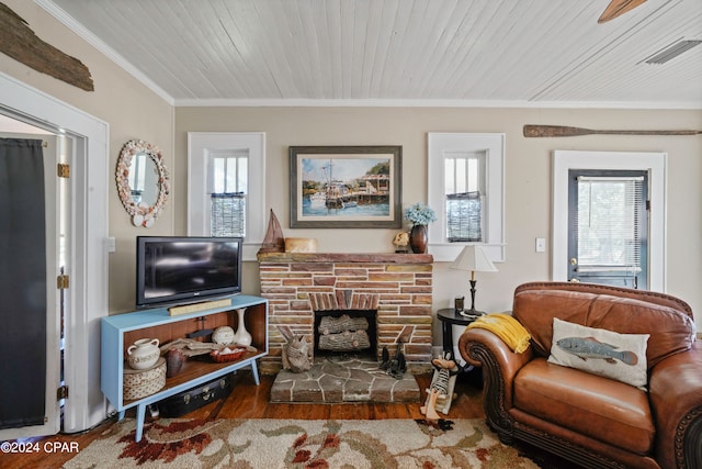 living room with hardwood / wood-style flooring, crown molding, a healthy amount of sunlight, and a stone fireplace