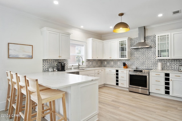 kitchen with white cabinets, wall chimney exhaust hood, a breakfast bar, stainless steel electric stove, and decorative light fixtures