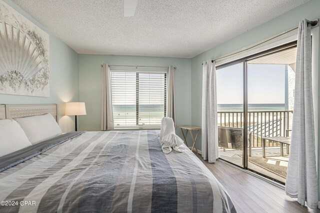 bedroom featuring hardwood / wood-style floors, a textured ceiling, access to outside, and a water view