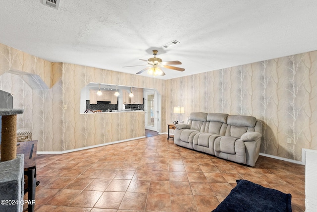 living room with a textured ceiling, visible vents, a ceiling fan, baseboards, and wallpapered walls