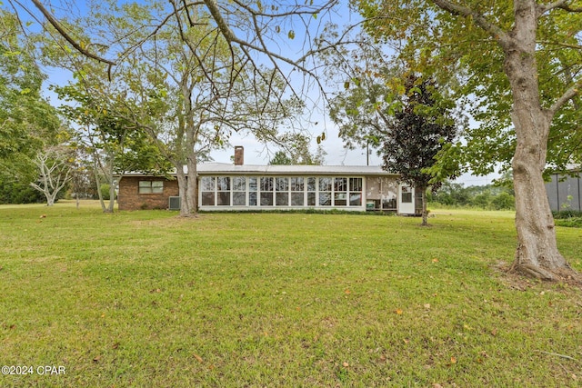 rear view of house featuring a sunroom, a chimney, and a lawn