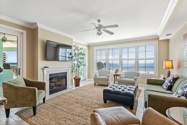 living room with light tile patterned floors, ceiling fan, ornamental molding, and a tiled fireplace