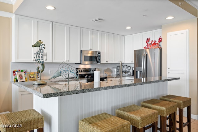 kitchen with stone counters, white cabinetry, sink, a kitchen bar, and appliances with stainless steel finishes