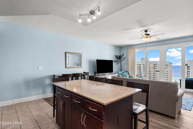 kitchen featuring light wood-type flooring, a kitchen island, dark brown cabinets, a kitchen breakfast bar, and ceiling fan