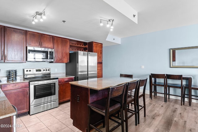 kitchen with a kitchen island, a breakfast bar area, stainless steel appliances, light stone countertops, and light hardwood / wood-style floors