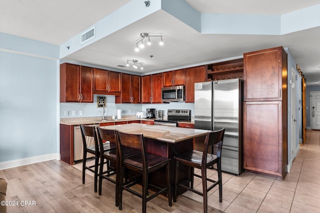 kitchen with light stone countertops, appliances with stainless steel finishes, a barn door, a breakfast bar, and light hardwood / wood-style flooring