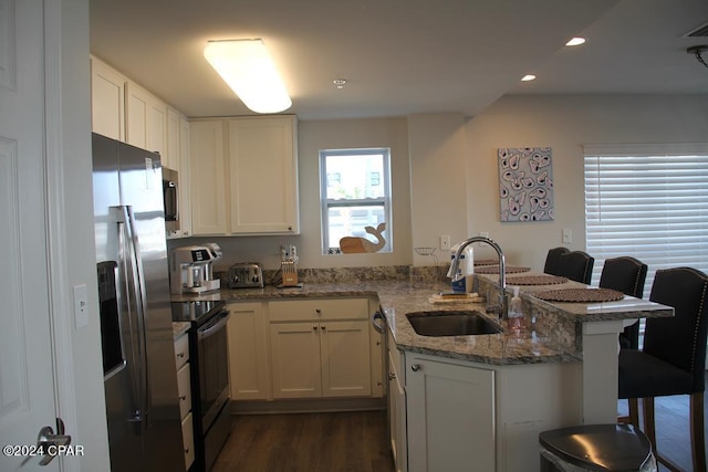 kitchen with light stone countertops, appliances with stainless steel finishes, a kitchen breakfast bar, sink, and white cabinetry