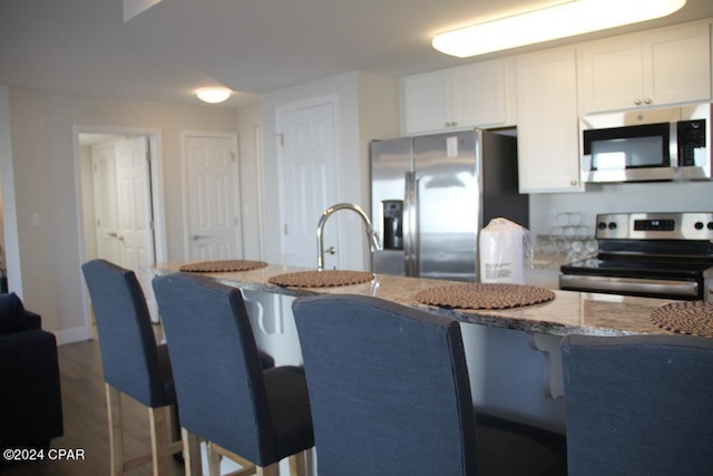 kitchen featuring dark wood-type flooring, light stone countertops, a kitchen bar, white cabinetry, and stainless steel appliances