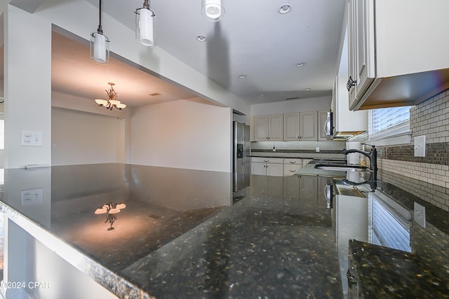 kitchen with backsplash, dark stone countertops, sink, decorative light fixtures, and appliances with stainless steel finishes