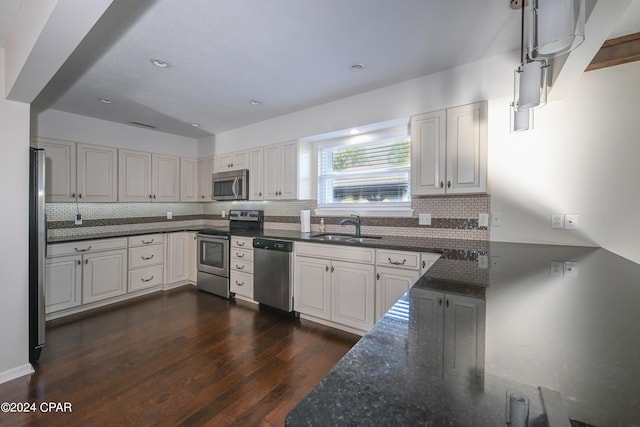 kitchen featuring decorative backsplash, appliances with stainless steel finishes, dark wood-type flooring, a sink, and dark stone countertops