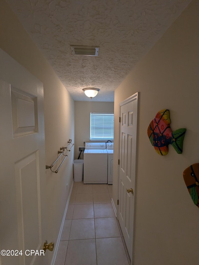 hall with light tile patterned floors, a textured ceiling, and washing machine and clothes dryer