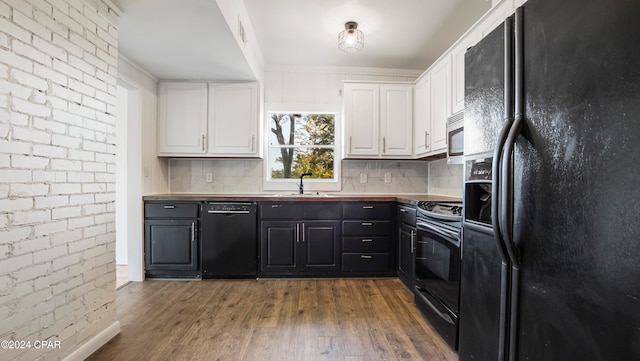 kitchen featuring black appliances, sink, hardwood / wood-style flooring, white cabinetry, and brick wall