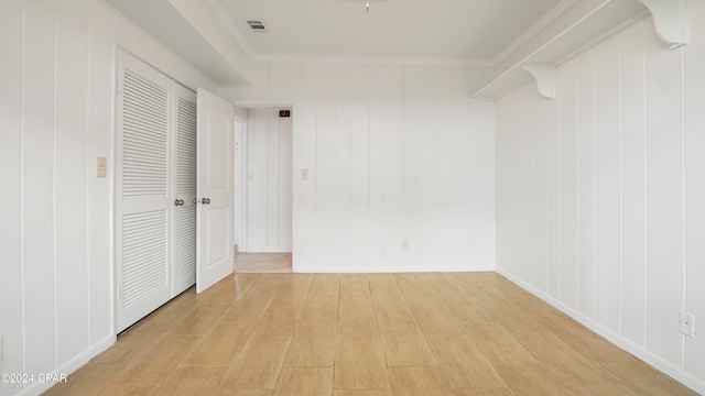 unfurnished bedroom featuring crown molding, wooden walls, and light hardwood / wood-style floors