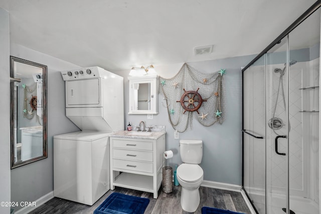 bathroom featuring hardwood / wood-style floors, stacked washing maching and dryer, vanity, an enclosed shower, and toilet