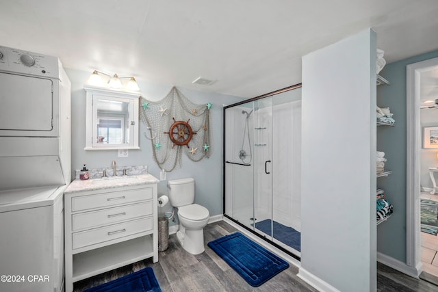 bathroom featuring stacked washer / dryer, a shower with door, vanity, hardwood / wood-style flooring, and toilet