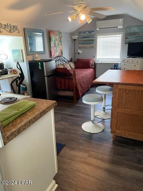 bedroom featuring dark hardwood / wood-style flooring, black fridge, a wall unit AC, and vaulted ceiling