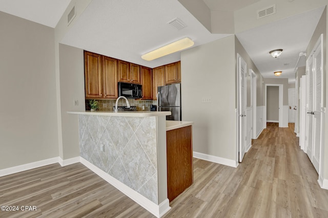 kitchen with kitchen peninsula, stainless steel fridge, light wood-type flooring, and backsplash