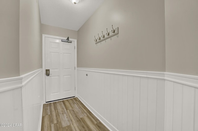 doorway to outside featuring light hardwood / wood-style flooring, a textured ceiling, and vaulted ceiling